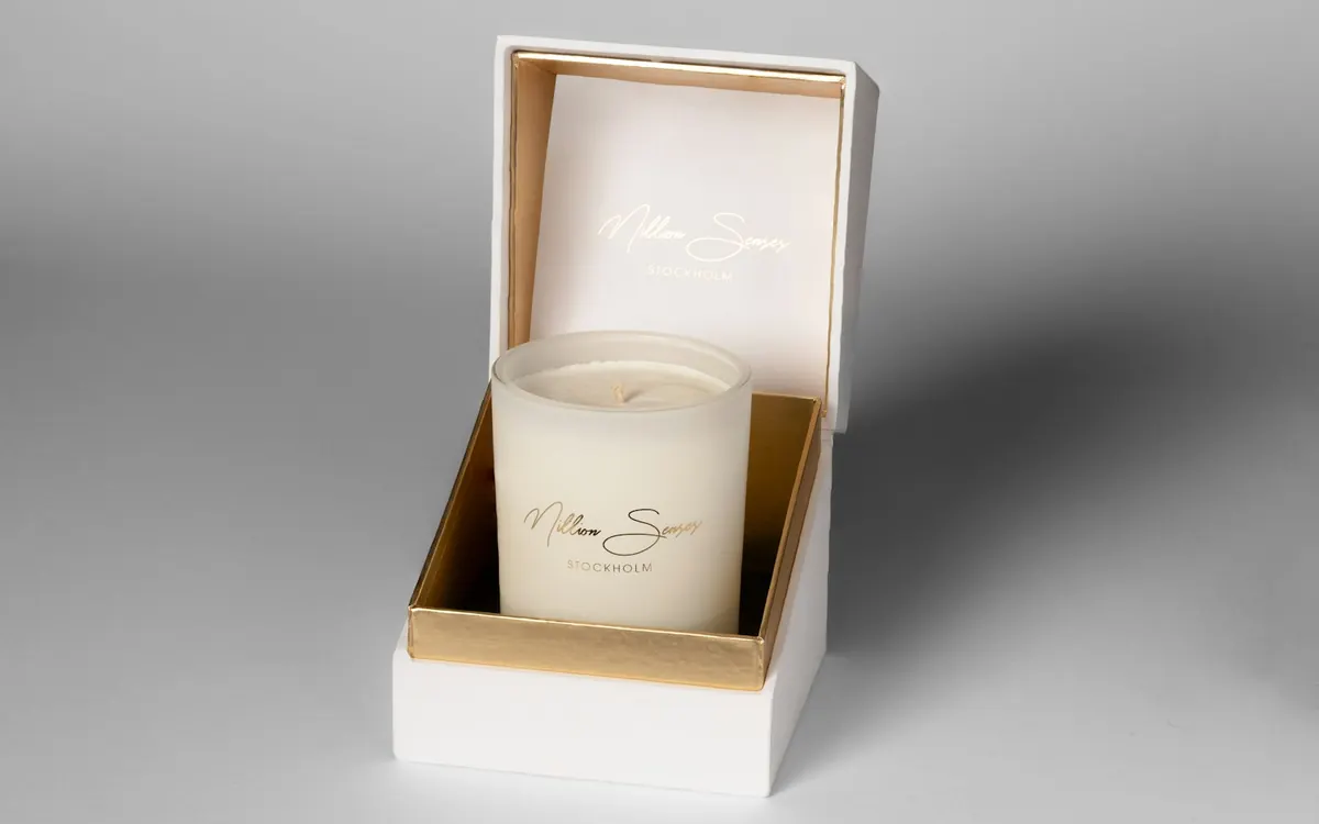 A white candle in an open white-and-gold gift box.