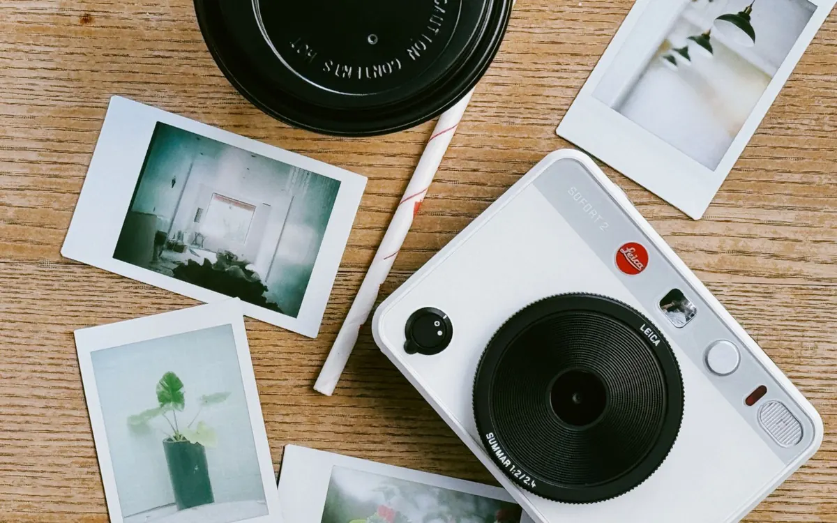 An instant camera with printed snapshots on a wooden table.