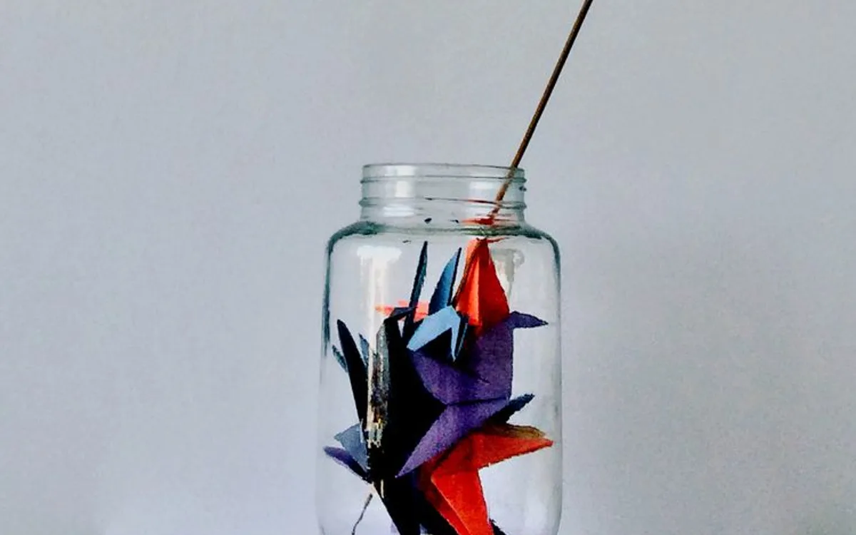 Small folded paper cranes displayed inside a glass jar.