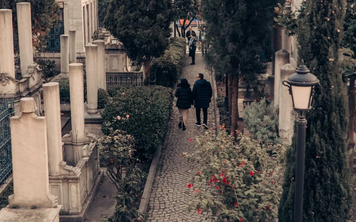Two people walking along a tree-lined park path.