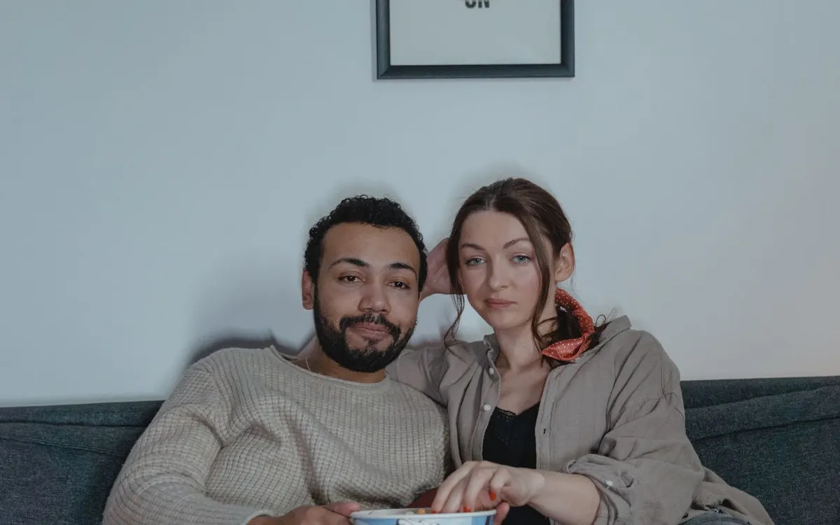 A couple watching a film on their sofa with popcorn.