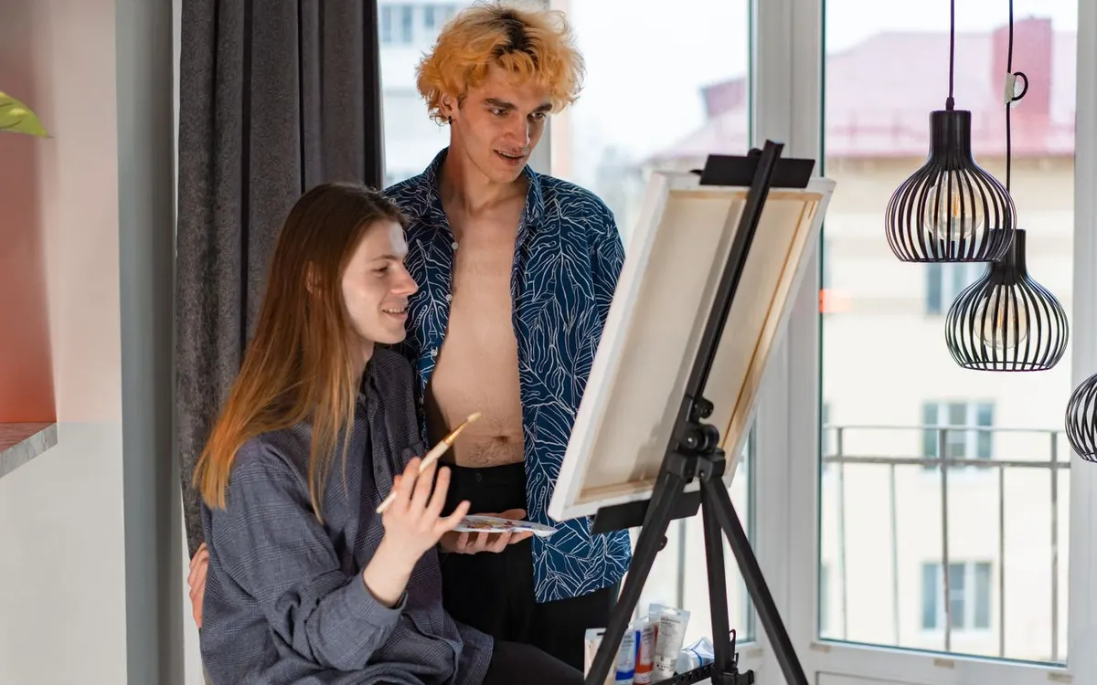 A couple painting together on a canvas indoors.