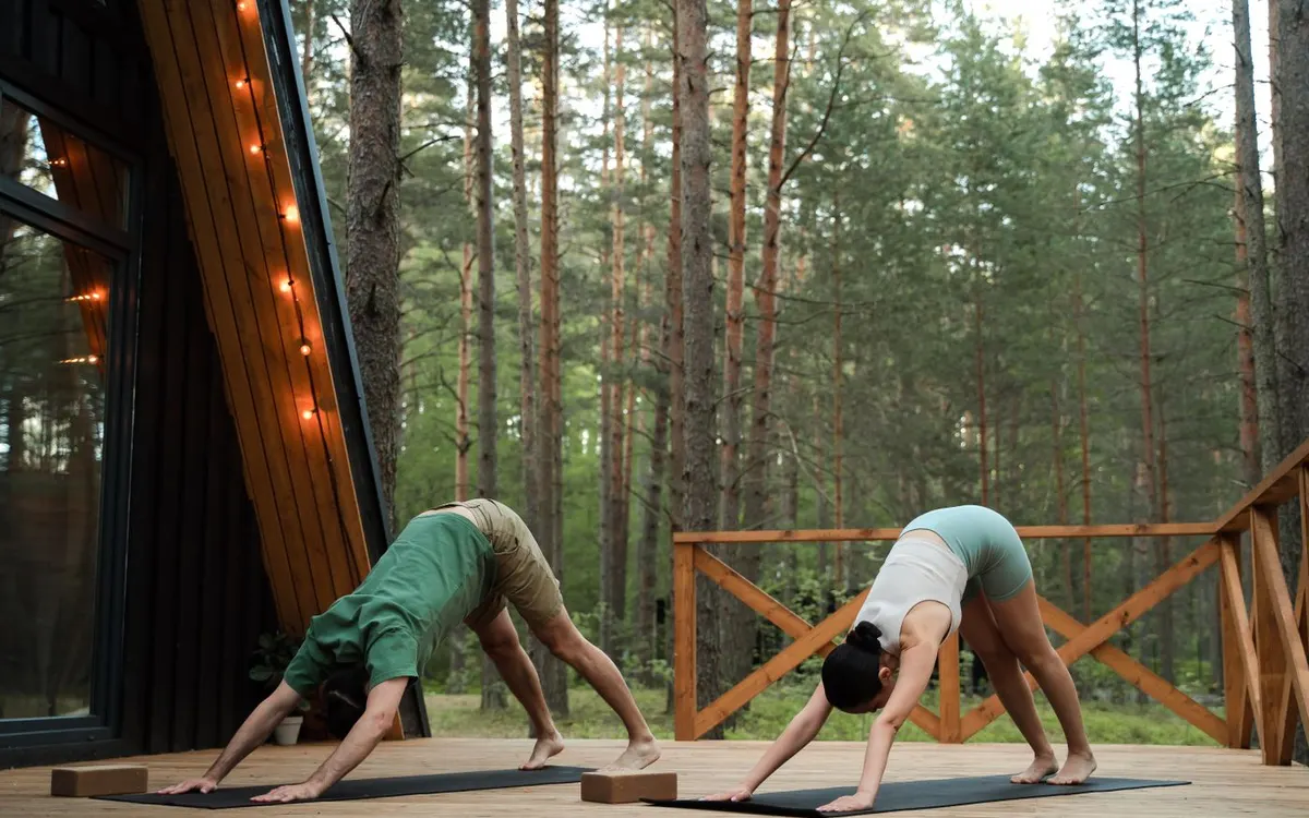 Two people practising yoga on a forest cabin deck.