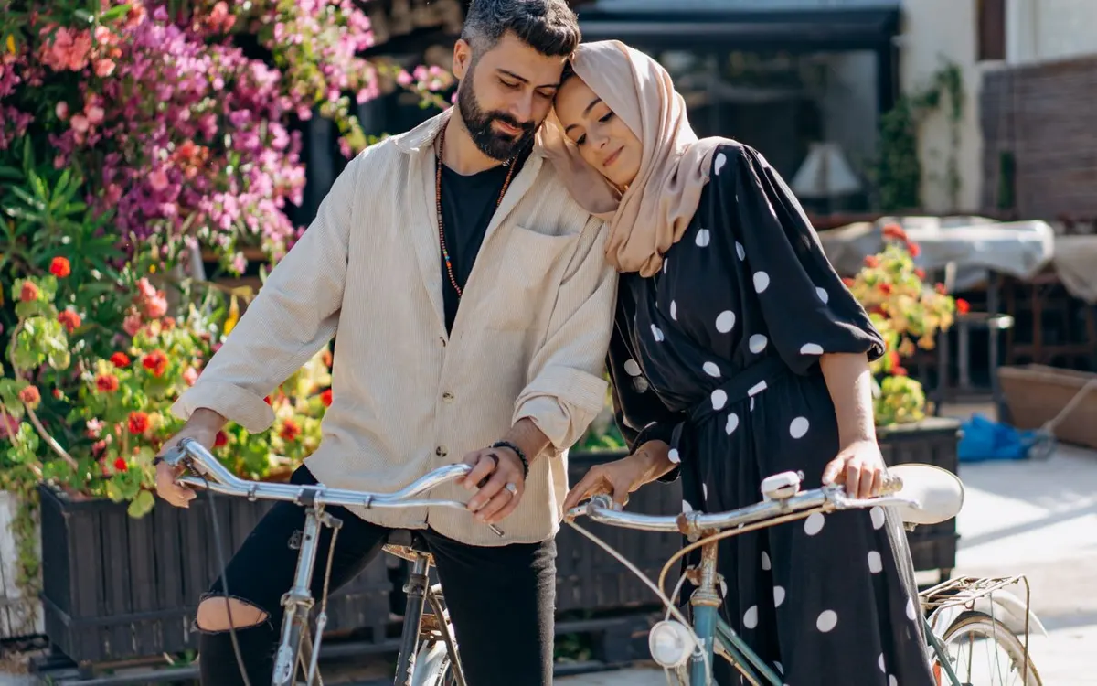 Two people riding bicycles together beside flowers.