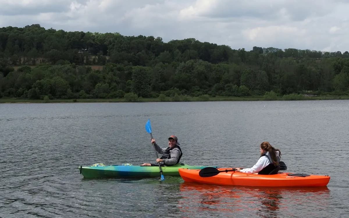 Two people paddling kayaks on a tree-lined river.
