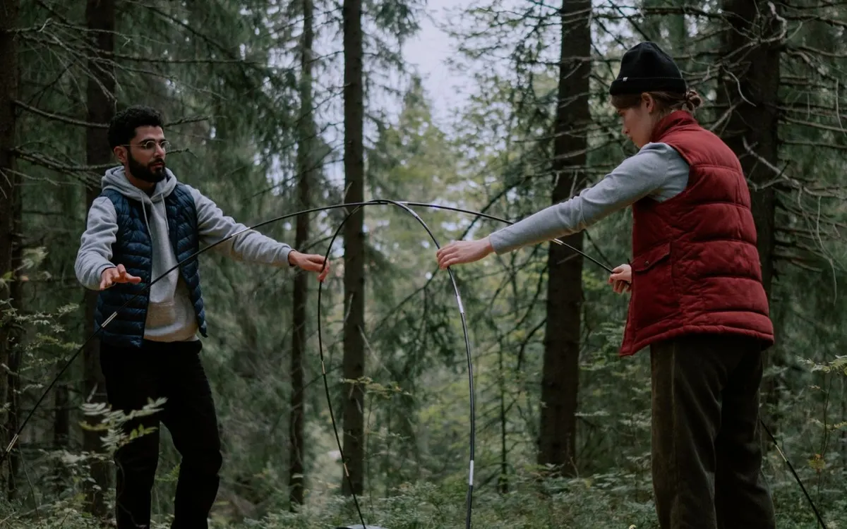 Two people setting up a tent in a forest.