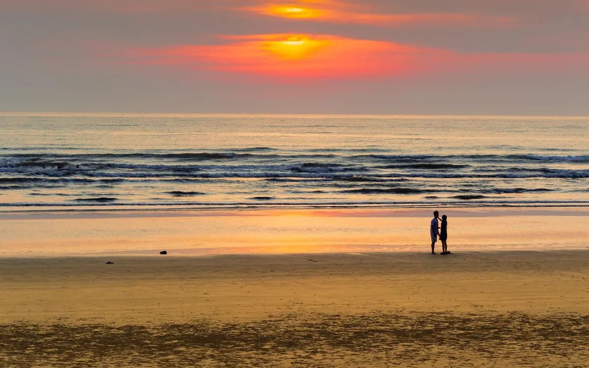 Two people standing on a beach at sunset.