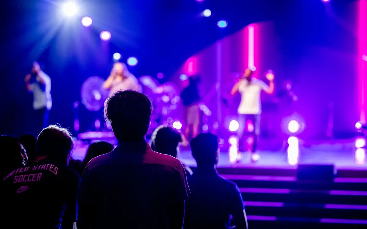 An audience watching a live performance under colourful stage lights.