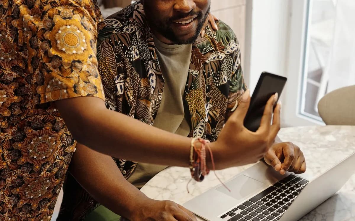 Two people using a laptop and phone for a kitchen video call.