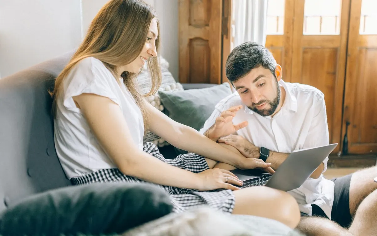 Two people sharing a laptop during a video call at home.