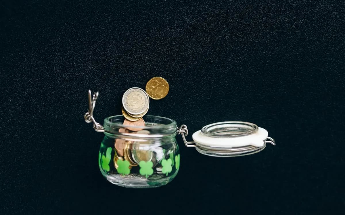 Coins falling into a clear glass savings jar.