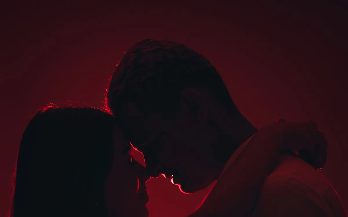 The silhouettes of two adults embracing in warm red light.