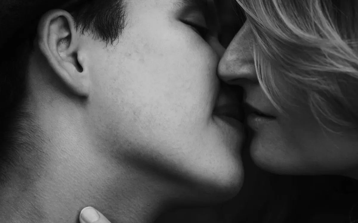 A black-and-white portrait of an adult couple sharing a kiss.