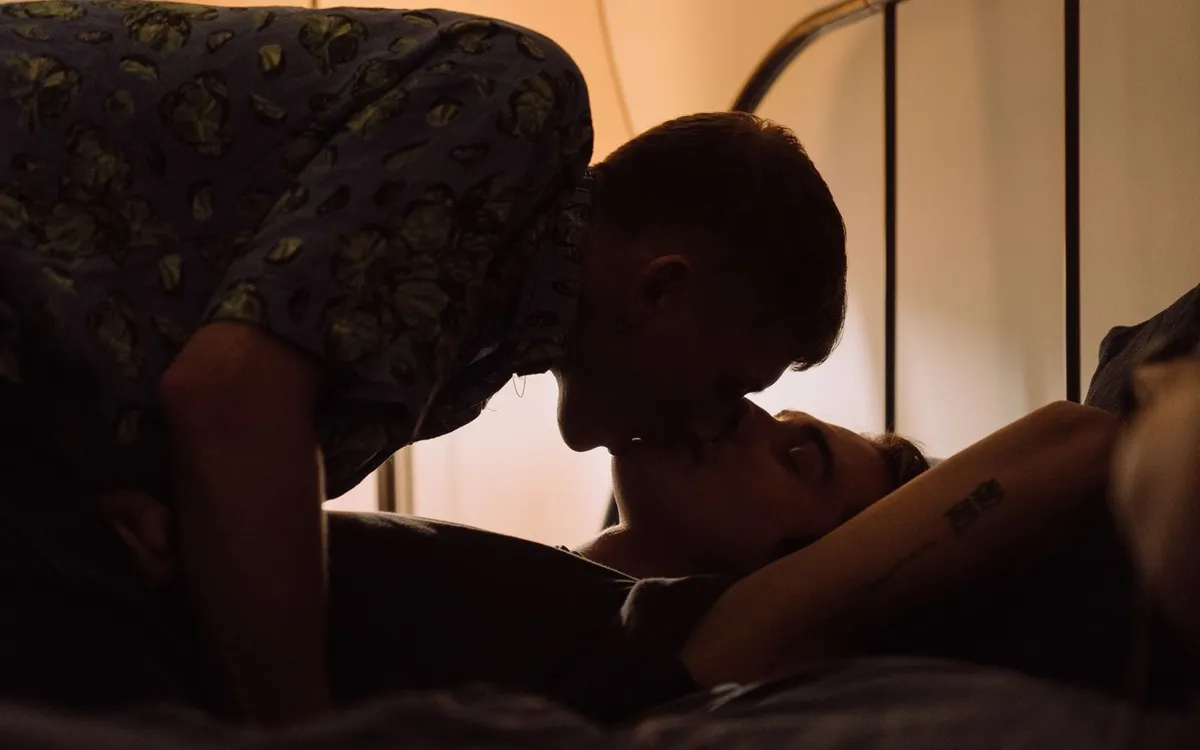 Two adult men kissing in a softly lit room.
