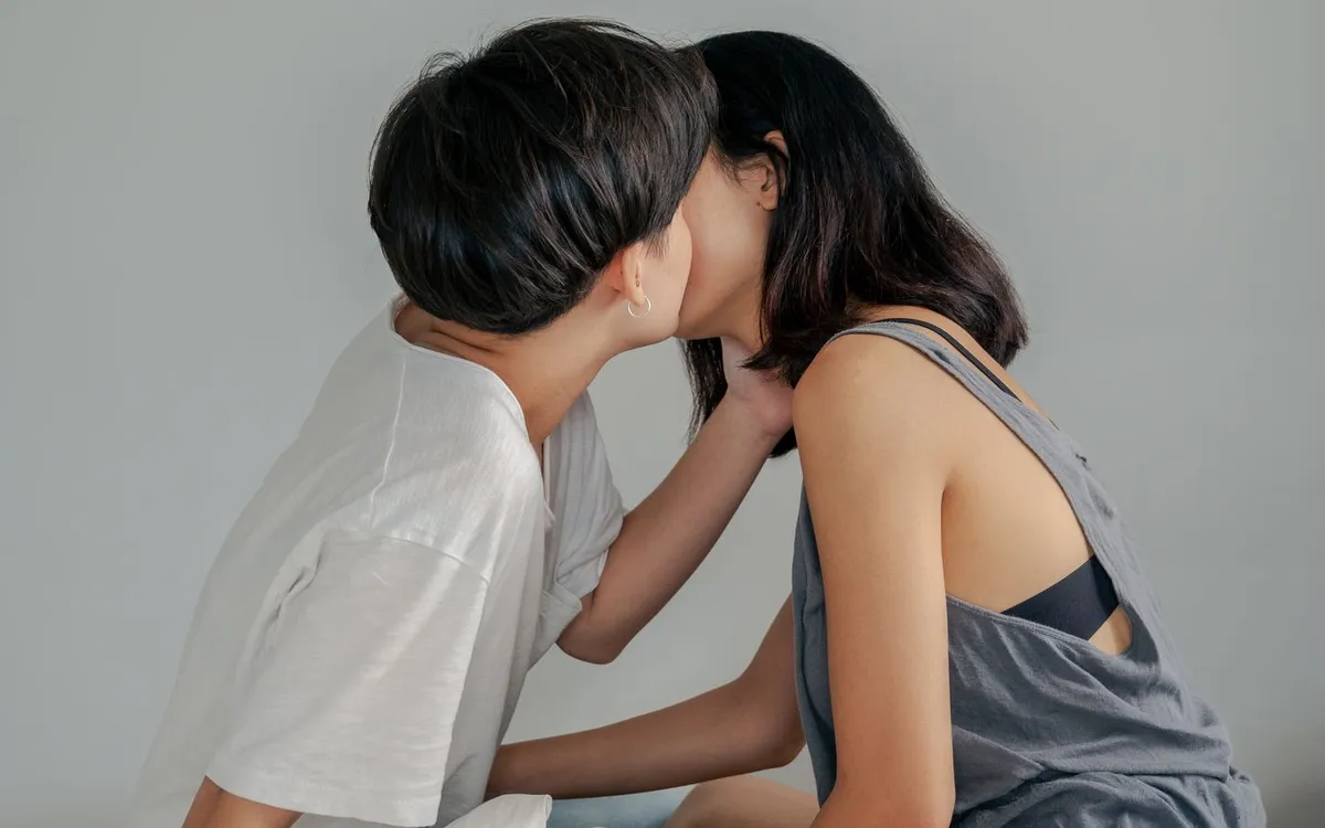 An adult couple sharing a kiss while seated on a bed.